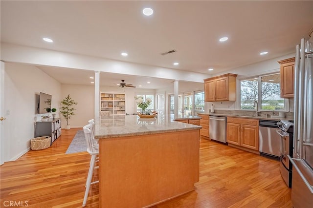 kitchen with appliances with stainless steel finishes, a breakfast bar, light wood-type flooring, a kitchen island, and ornate columns