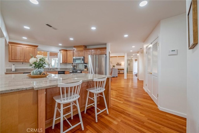 kitchen featuring appliances with stainless steel finishes, sink, light hardwood / wood-style flooring, light stone counters, and a kitchen breakfast bar