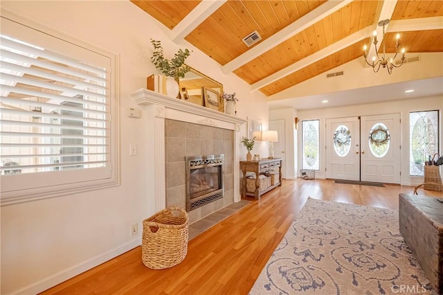 entryway with light wood-type flooring, wood ceiling, a tile fireplace, vaulted ceiling with beams, and a chandelier