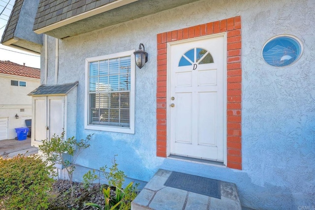 property entrance with a shingled roof and stucco siding