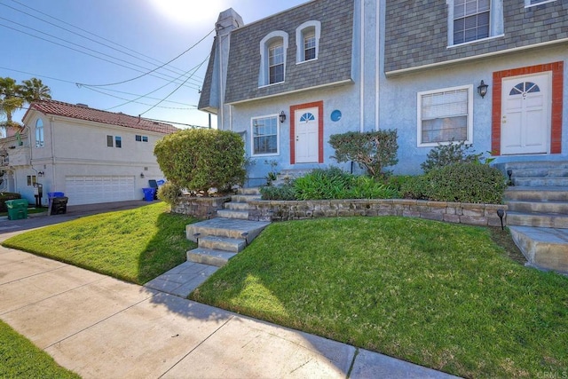 view of front facade with entry steps, mansard roof, roof with shingles, and stucco siding