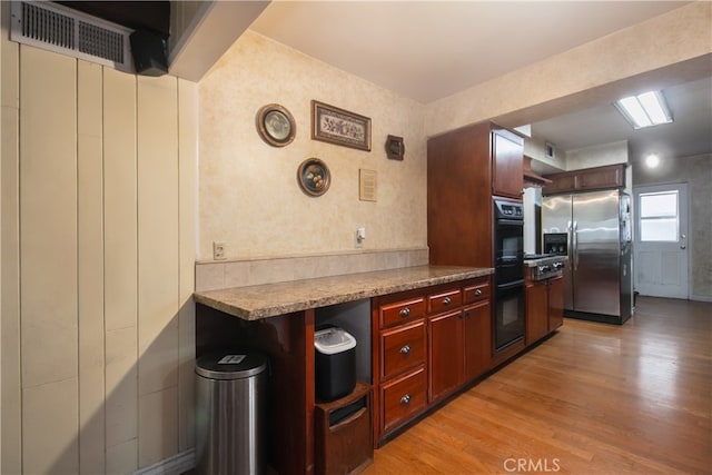 kitchen featuring light wood-type flooring, black double oven, and stainless steel fridge