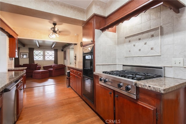 kitchen with light wood-type flooring, ceiling fan, light stone counters, appliances with stainless steel finishes, and decorative backsplash