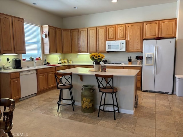 kitchen featuring brown cabinets, light countertops, a kitchen island, white appliances, and a kitchen bar