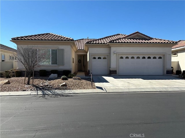 mediterranean / spanish-style home with a garage, concrete driveway, a tiled roof, and stucco siding