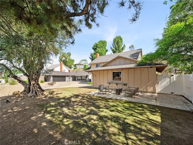 rear view of house with board and batten siding, a patio area, fence, and a chimney