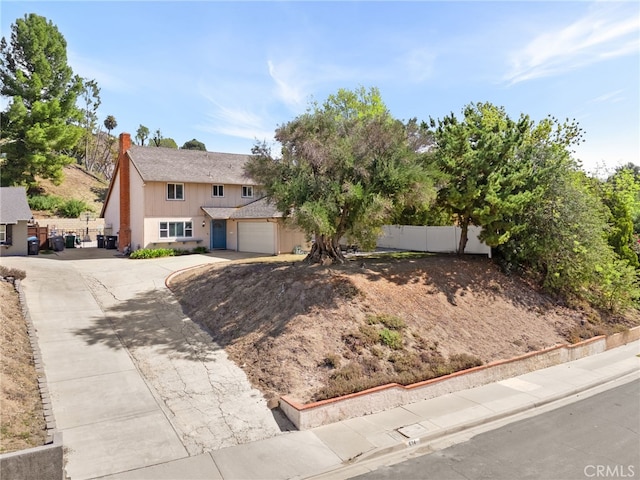 view of front of home featuring concrete driveway, a chimney, an attached garage, and fence