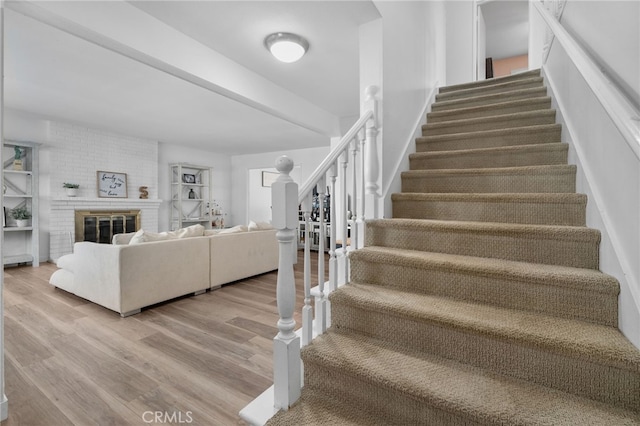 staircase with a fireplace, wood finished floors, and beamed ceiling