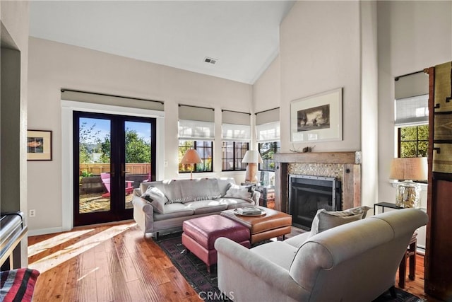 living area with high vaulted ceiling, a wealth of natural light, hardwood / wood-style flooring, and visible vents