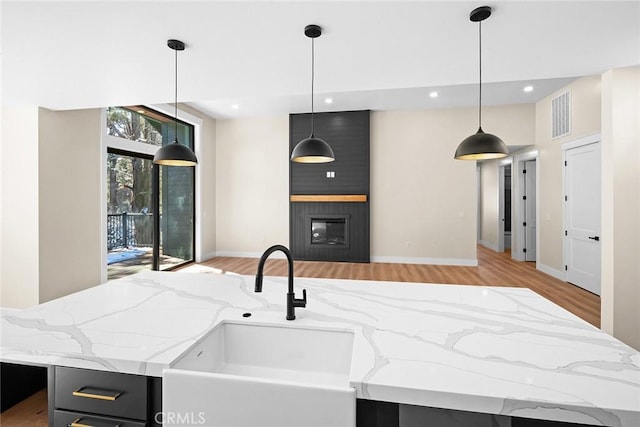 kitchen featuring a fireplace, sink, hanging light fixtures, light stone counters, and a center island with sink