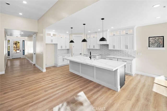 kitchen featuring light stone countertops, a kitchen island with sink, white cabinets, and light hardwood / wood-style flooring