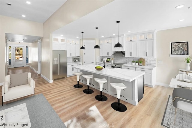 kitchen featuring a kitchen island with sink, stainless steel appliances, light stone counters, white cabinets, and decorative light fixtures