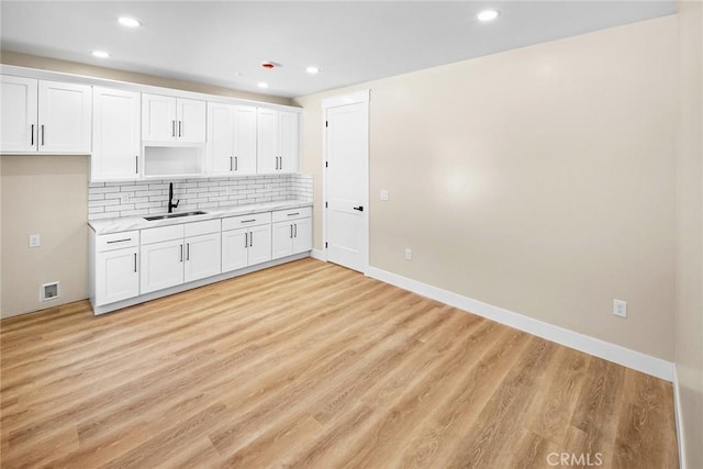 kitchen with sink, backsplash, white cabinets, and light wood-type flooring