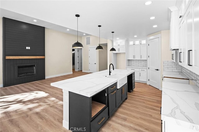 kitchen featuring a fireplace, decorative light fixtures, sink, white cabinets, and a large island