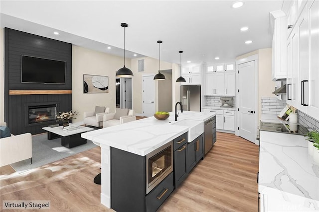 kitchen with pendant lighting, built in microwave, white cabinetry, high end refrigerator, and a kitchen island with sink