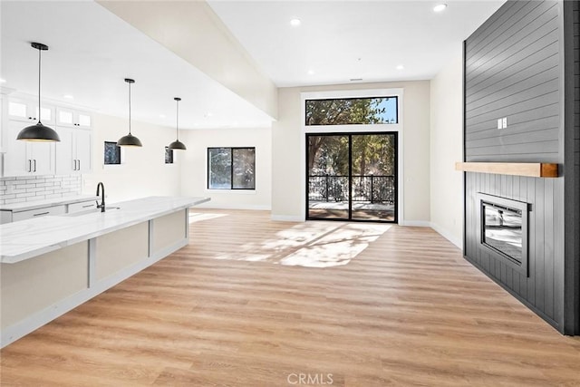 interior space featuring white cabinetry, backsplash, hanging light fixtures, and light hardwood / wood-style flooring