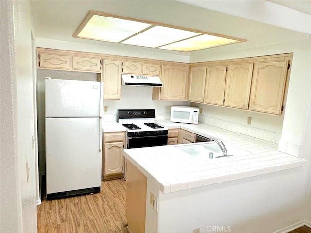 kitchen with white appliances, sink, light hardwood / wood-style floors, kitchen peninsula, and tile counters