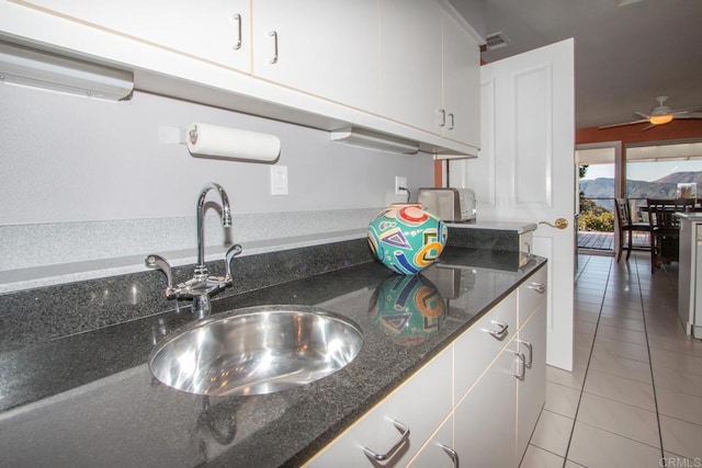 kitchen featuring light tile patterned flooring, sink, white cabinetry, ceiling fan, and dark stone counters