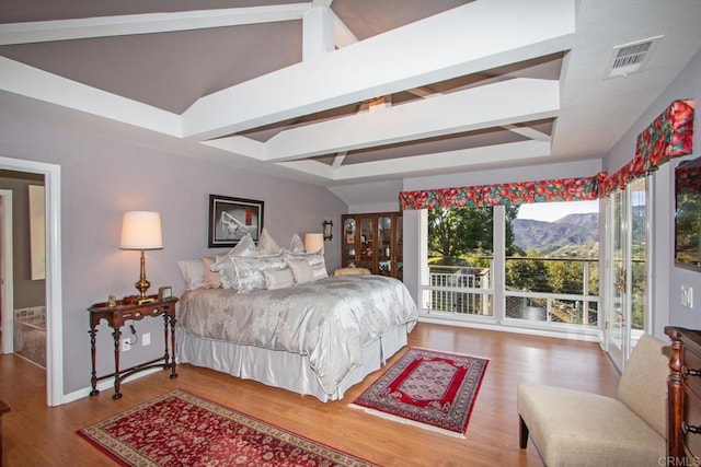 bedroom with a mountain view, a tray ceiling, wood-type flooring, and beamed ceiling