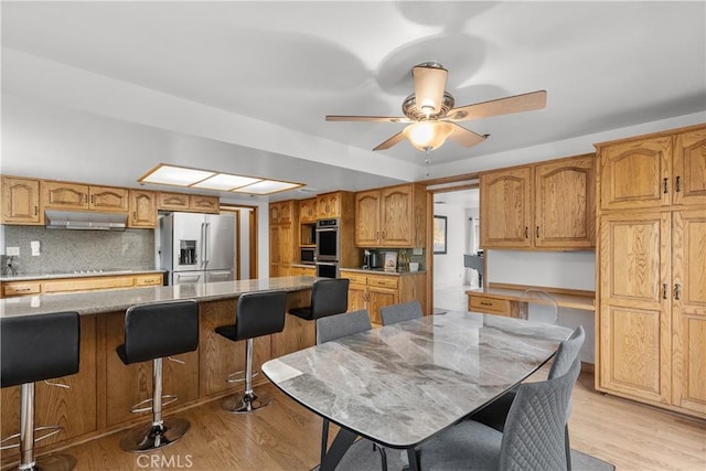 kitchen featuring light wood-type flooring, a breakfast bar, ceiling fan, appliances with stainless steel finishes, and decorative backsplash