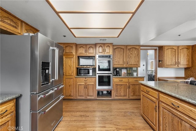 kitchen with light hardwood / wood-style floors, appliances with stainless steel finishes, and light stone countertops