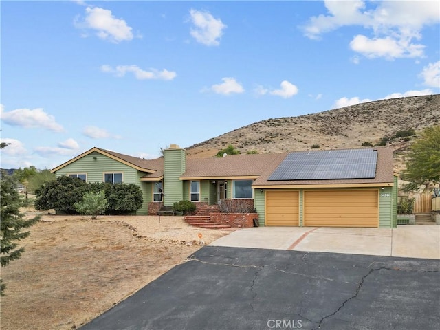 ranch-style home featuring a mountain view, a garage, and solar panels