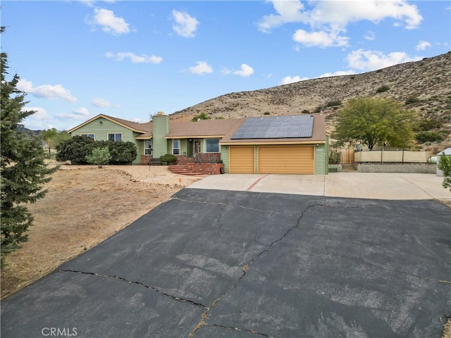 ranch-style house with a mountain view, a garage, and solar panels