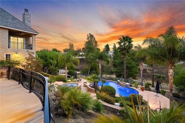 pool at dusk with a patio area and an outdoor pool