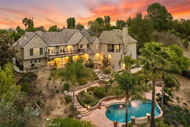 back of property at dusk featuring a chimney, a patio area, and a balcony