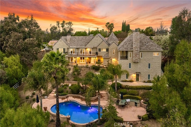 back of house at dusk featuring an outdoor pool, a patio, a balcony, a chimney, and stairway