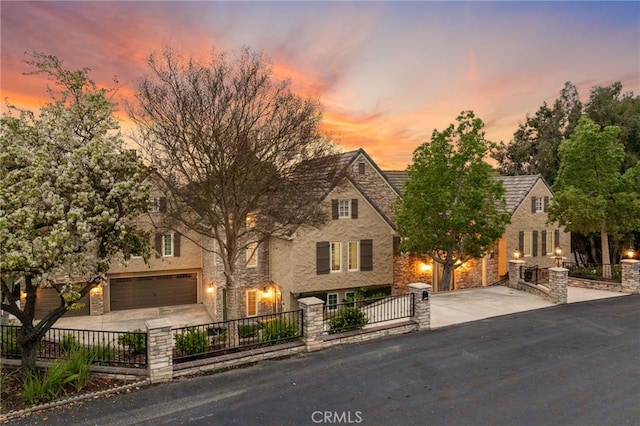 view of front of home featuring driveway, stone siding, a fenced front yard, and a garage