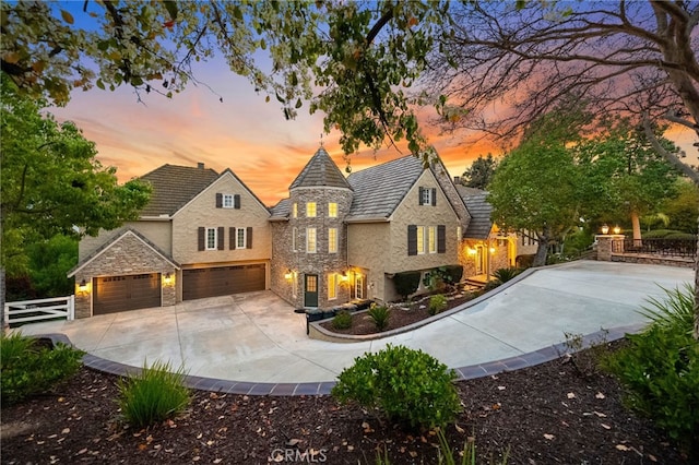 view of front facade featuring driveway, stone siding, an attached garage, fence, and stucco siding