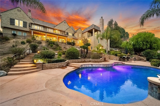 outdoor pool with a patio area, fence, and stairway