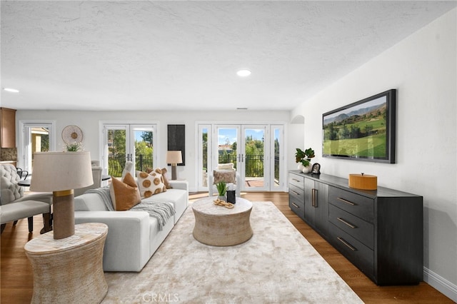 living room with a textured ceiling, arched walkways, wood finished floors, and french doors