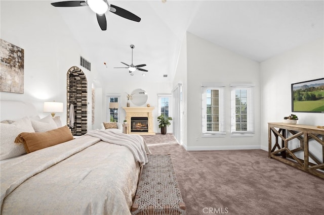 carpeted bedroom with high vaulted ceiling, a warm lit fireplace, multiple windows, and baseboards