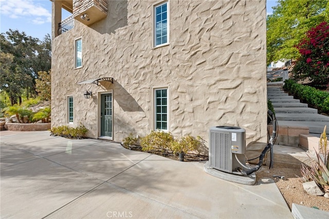 exterior space featuring a patio area, stairs, central AC, and stucco siding