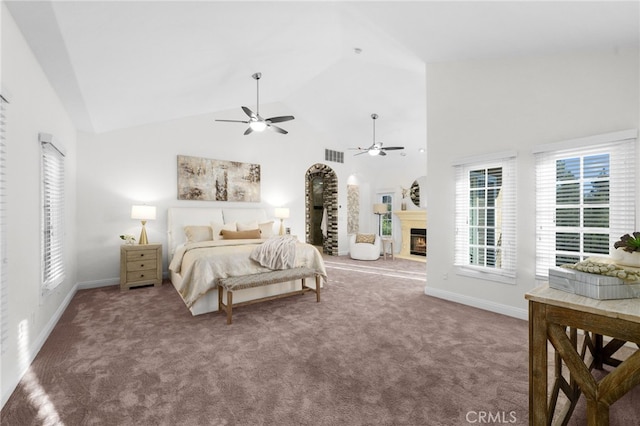 carpeted bedroom featuring a warm lit fireplace, high vaulted ceiling, a ceiling fan, visible vents, and baseboards