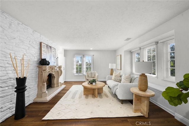 living area featuring a textured ceiling, a fireplace with raised hearth, dark wood-style flooring, visible vents, and baseboards