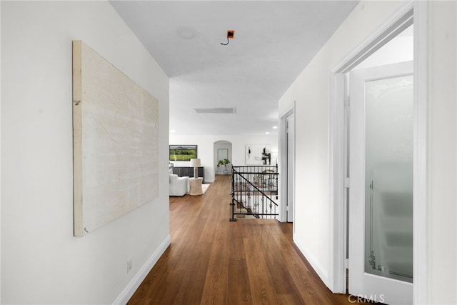 hallway featuring baseboards, arched walkways, wood finished floors, and an upstairs landing