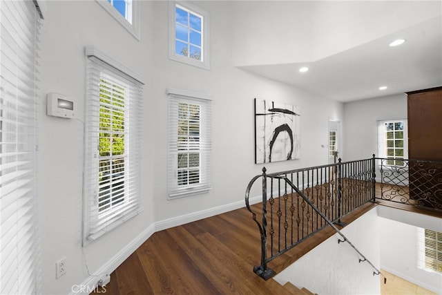 hallway featuring recessed lighting, a high ceiling, an upstairs landing, wood finished floors, and baseboards