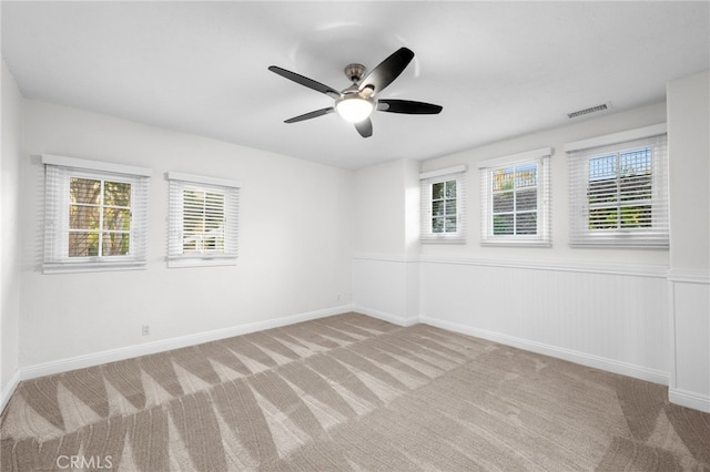 carpeted spare room featuring baseboards, visible vents, a ceiling fan, and wainscoting