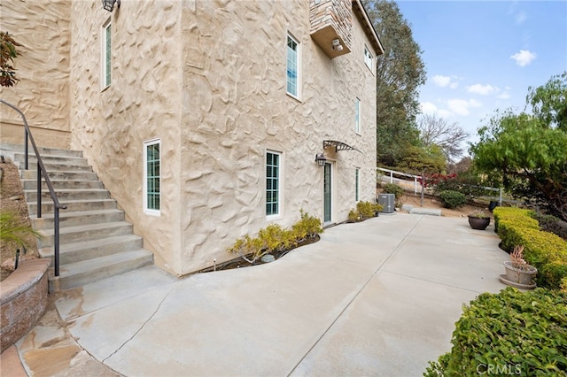 view of property exterior featuring stucco siding, a patio, stairway, and central AC unit