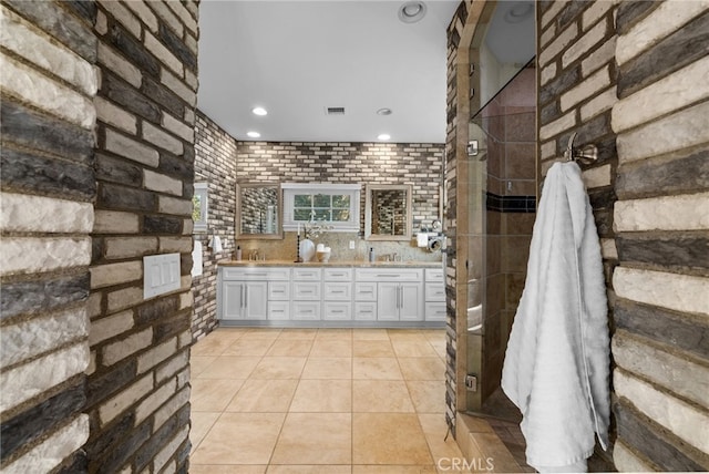 full bathroom with double vanity, a stall shower, a sink, brick wall, and tile patterned flooring