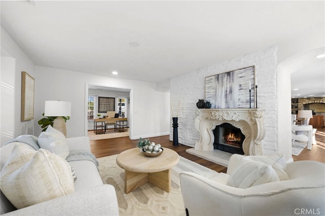 living area featuring a warm lit fireplace, baseboards, wood finished floors, and recessed lighting