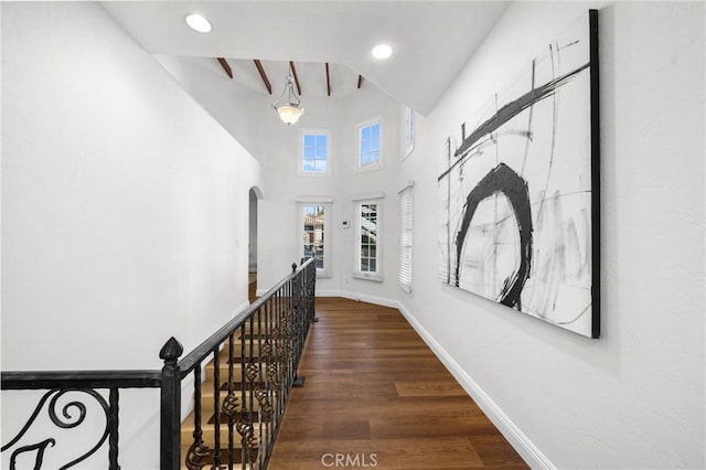 corridor with baseboards, arched walkways, wood finished floors, an upstairs landing, and recessed lighting