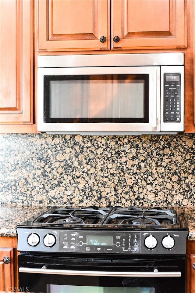 kitchen featuring stainless steel microwave, backsplash, light stone countertops, and black gas range oven