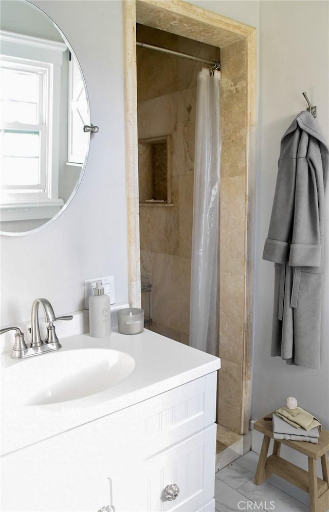 full bath featuring marble finish floor, a tile shower, and vanity