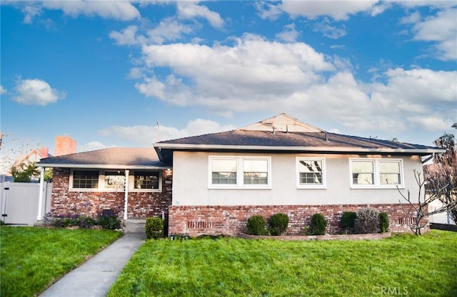 view of front of property featuring brick siding, fence, a gate, stucco siding, and a front yard