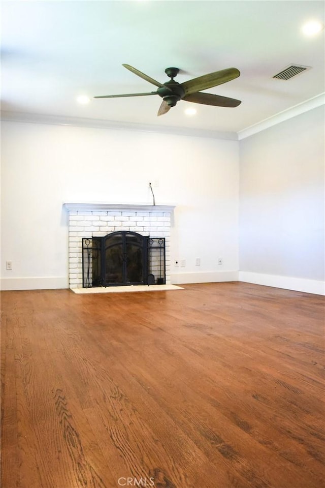 unfurnished living room featuring crown molding, a fireplace, visible vents, wood finished floors, and baseboards