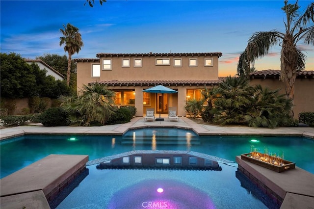 back house at dusk featuring a fire pit and a patio